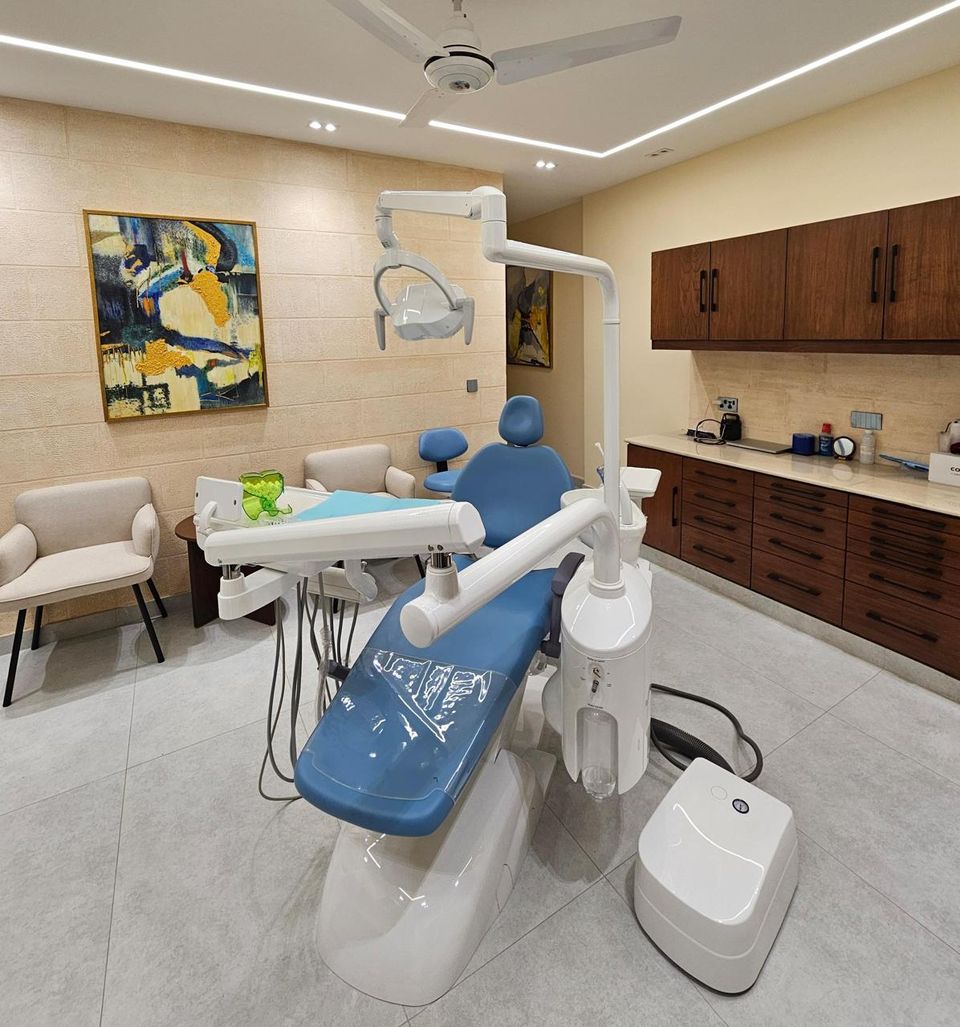 A dental treatment room with a blue patient chair, overhead light and cabinets