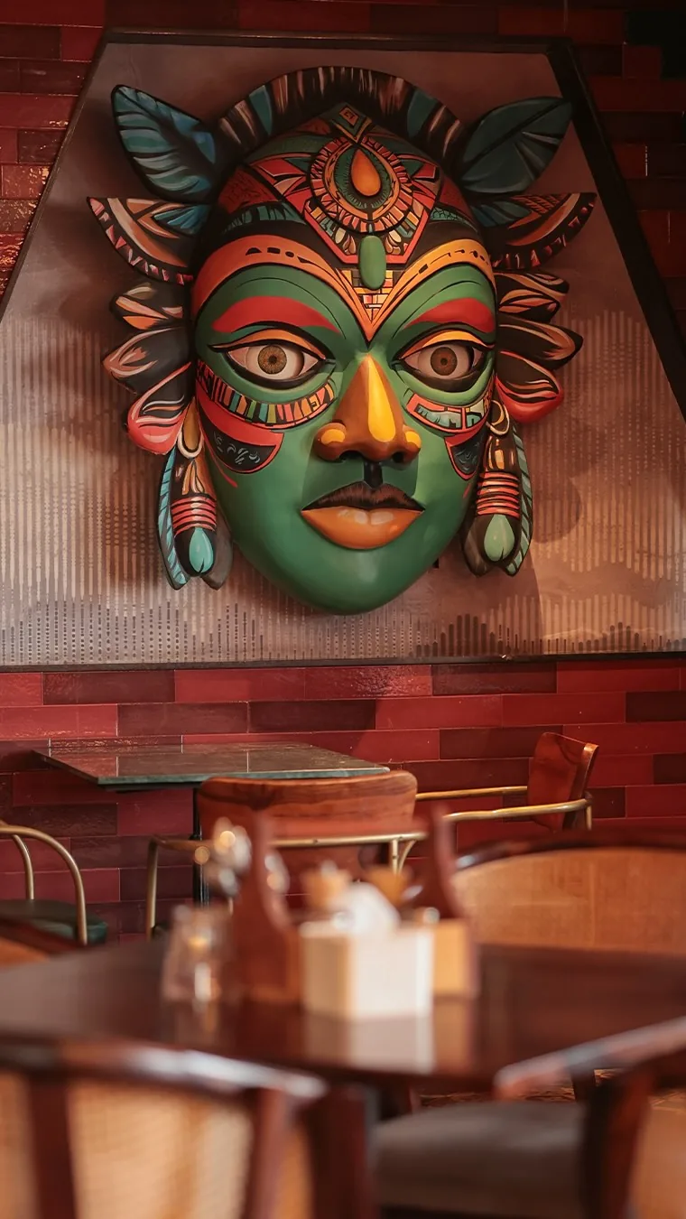 A hand-painted mask mounted on the red brick wall above the seating
