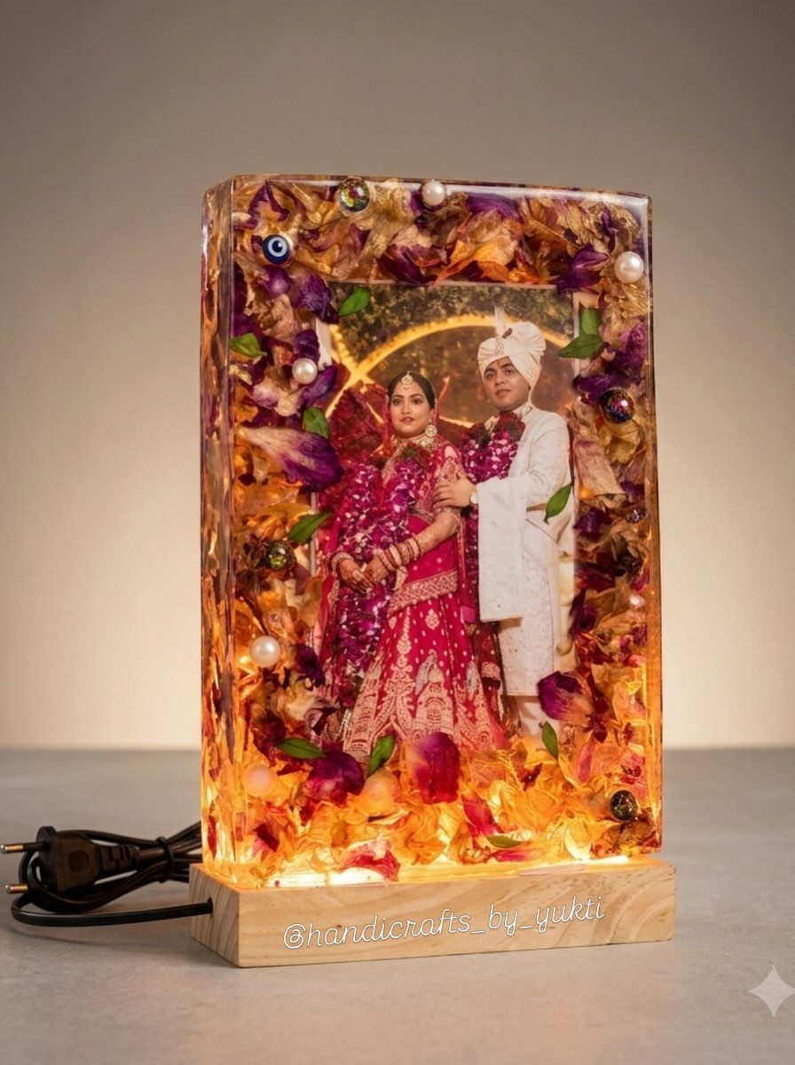 A resin frame holding a wedding photo, rose petals and pearls, glowing on a lit wooden base