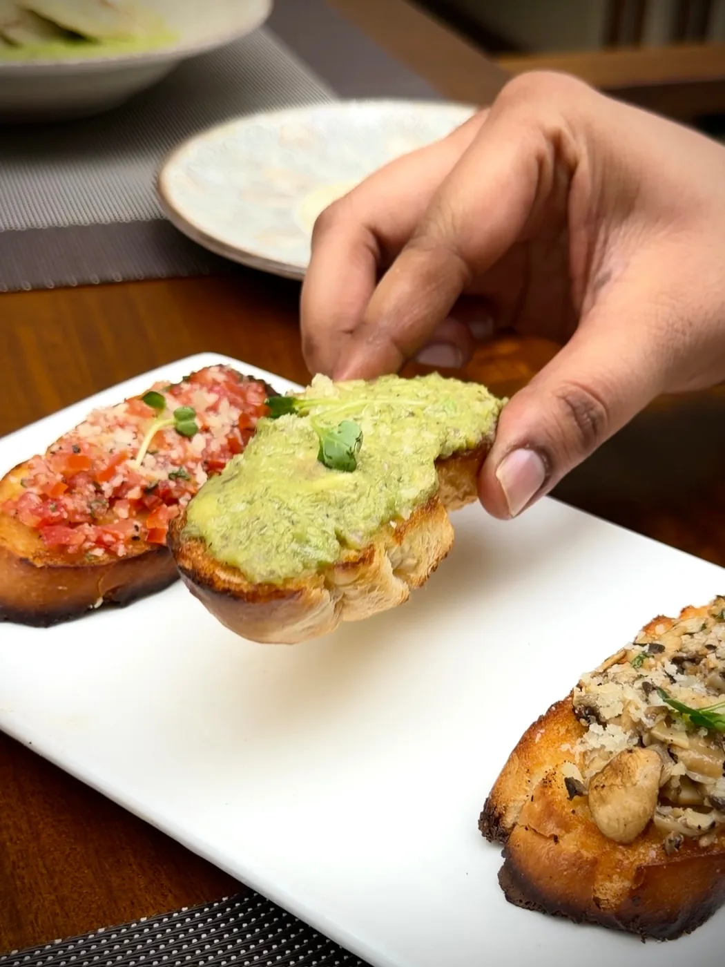 Three bruschetta on a white platter: tomato, avocado and mushroom