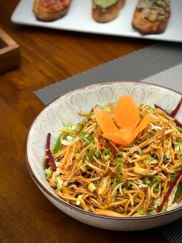 Bowl of hakka noodles garnished with a carved carrot flower and spring onion
