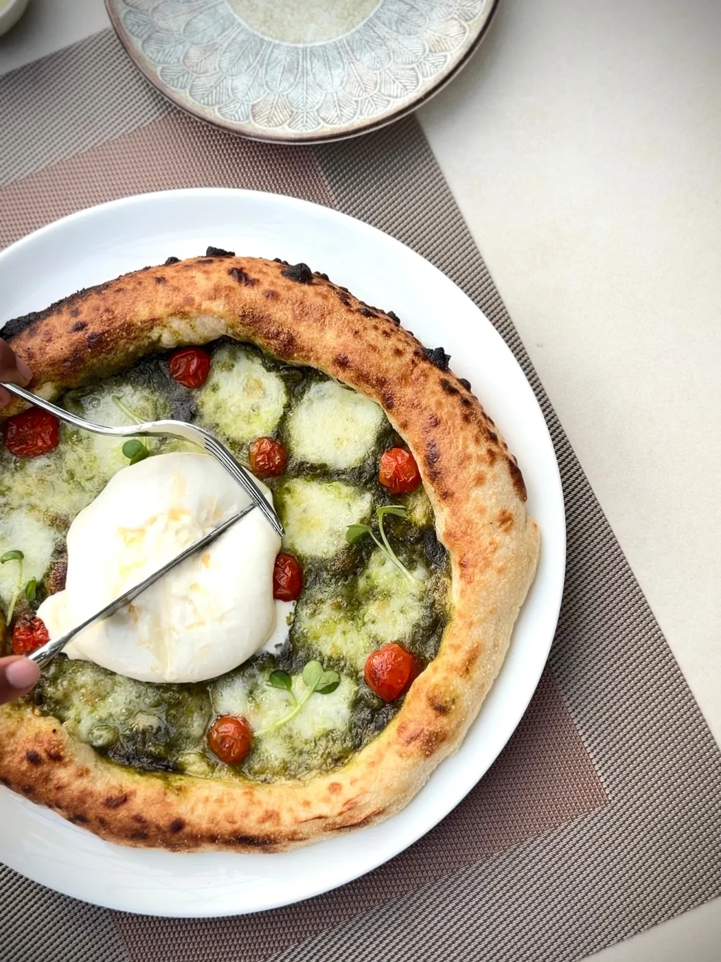 Wood-fired pesto pizza topped with burrata, confit cherry tomatoes and micro greens
