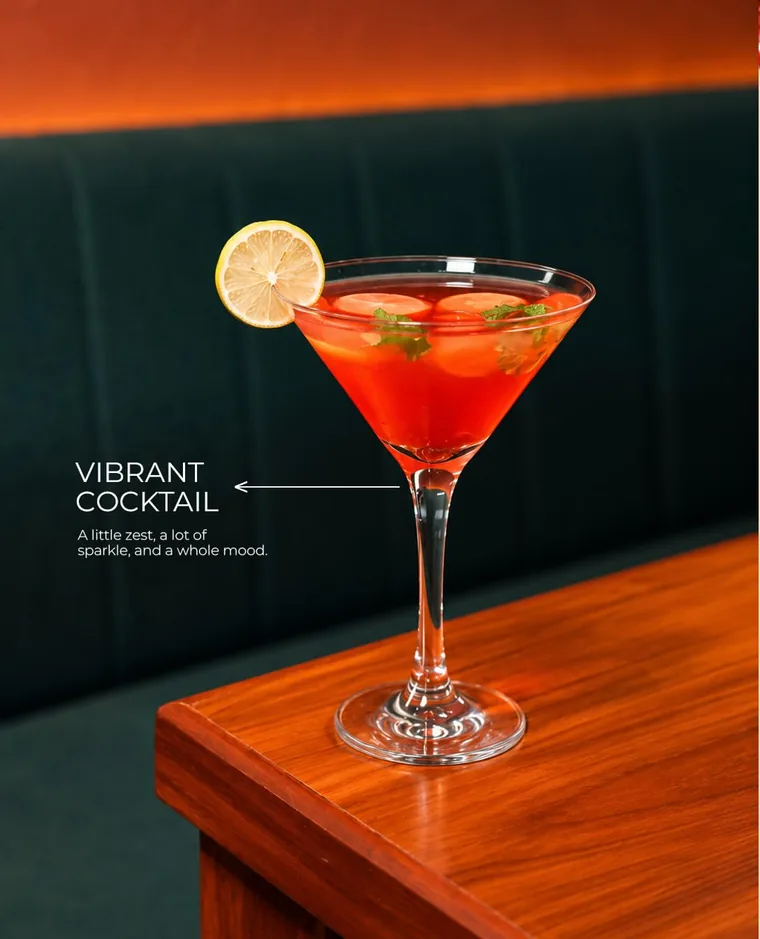 Red cocktail in a martini glass on a table beside the teal booth