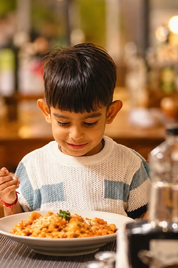 A child smiling over a bowl of pasta in the dining room