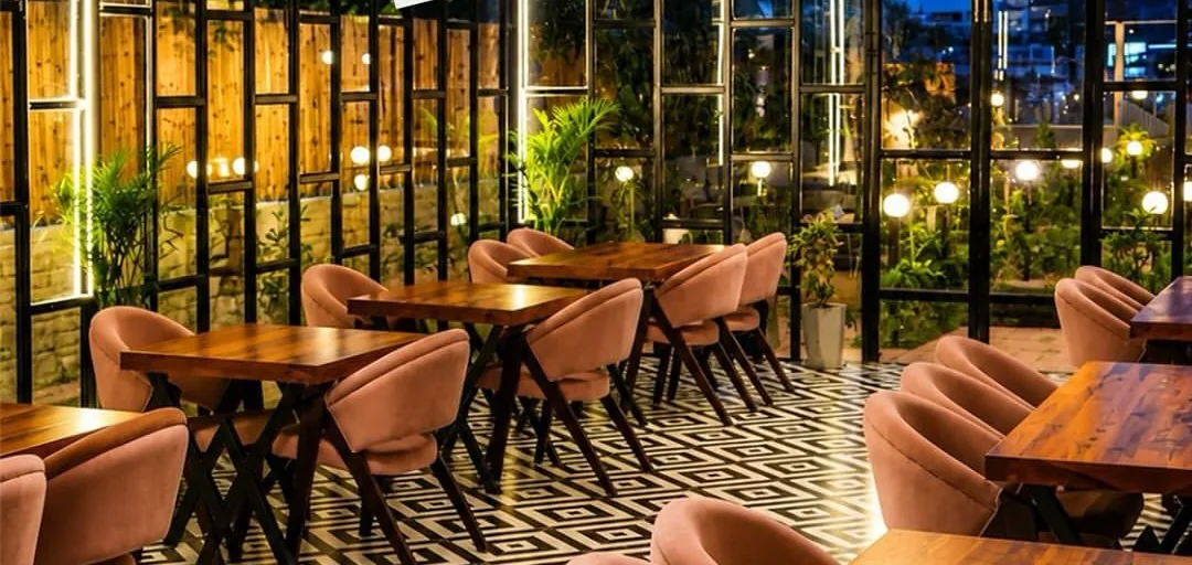 The dining room at Vaishali Veg Inn — wooden tables, blush chairs and warm lights along a glass wall