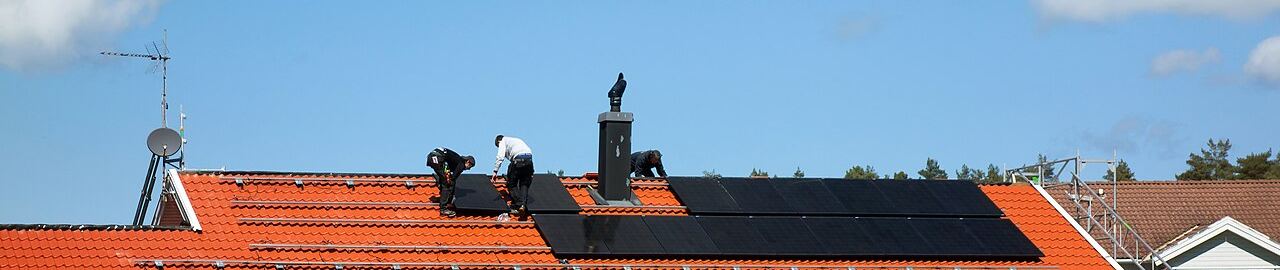 Installers fitting black solar panels on a roof