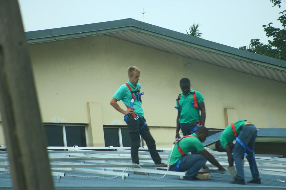 Installers in safety harnesses fitting solar panel frames on a roof